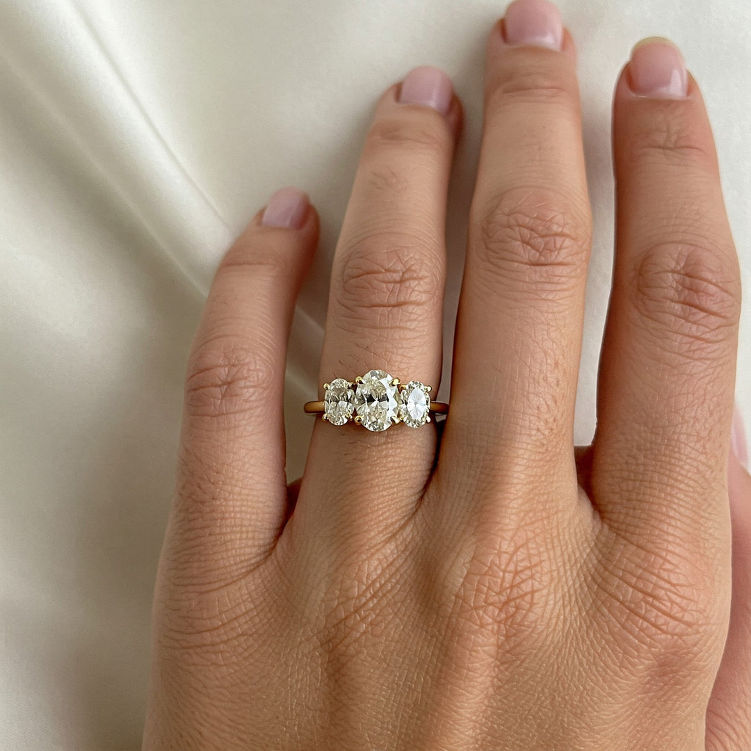 Three-stone diamond engagement ring on finger, gold band, oval center stone, perfect for Charlotte proposals
