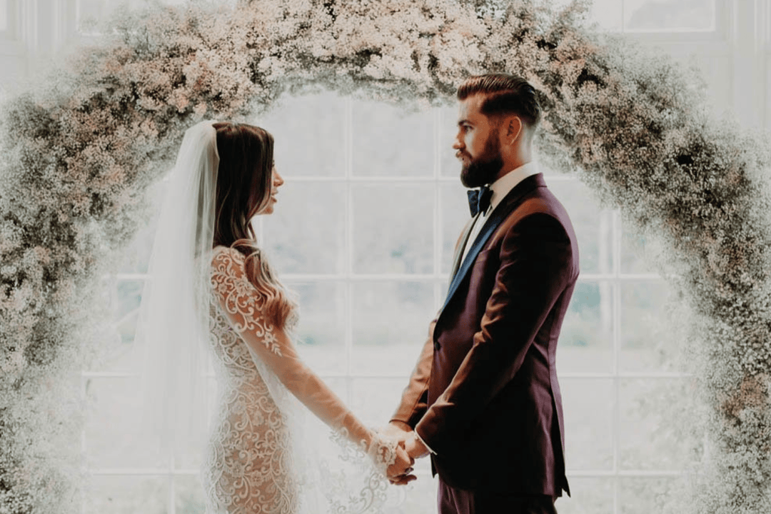 Bride and groom holding hands under floral arch, perfect for engagement rings and wedding jewelry