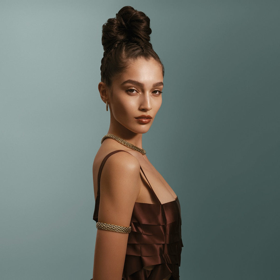 Elegant woman wearing gold chain necklace, matching earrings, and arm cuff, styled for luxury jewelry showcase