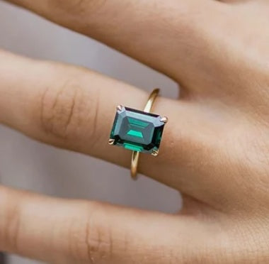 Emerald-cut green gemstone ring in gold setting on finger, elegant engagement or gemstone jewelry