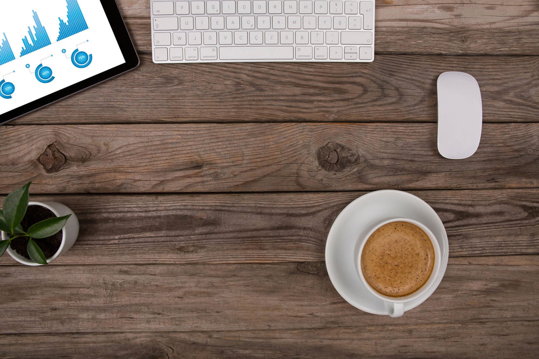 Wooden desk with laptop showing charts, keyboard, mouse, coffee cup, and small plant
