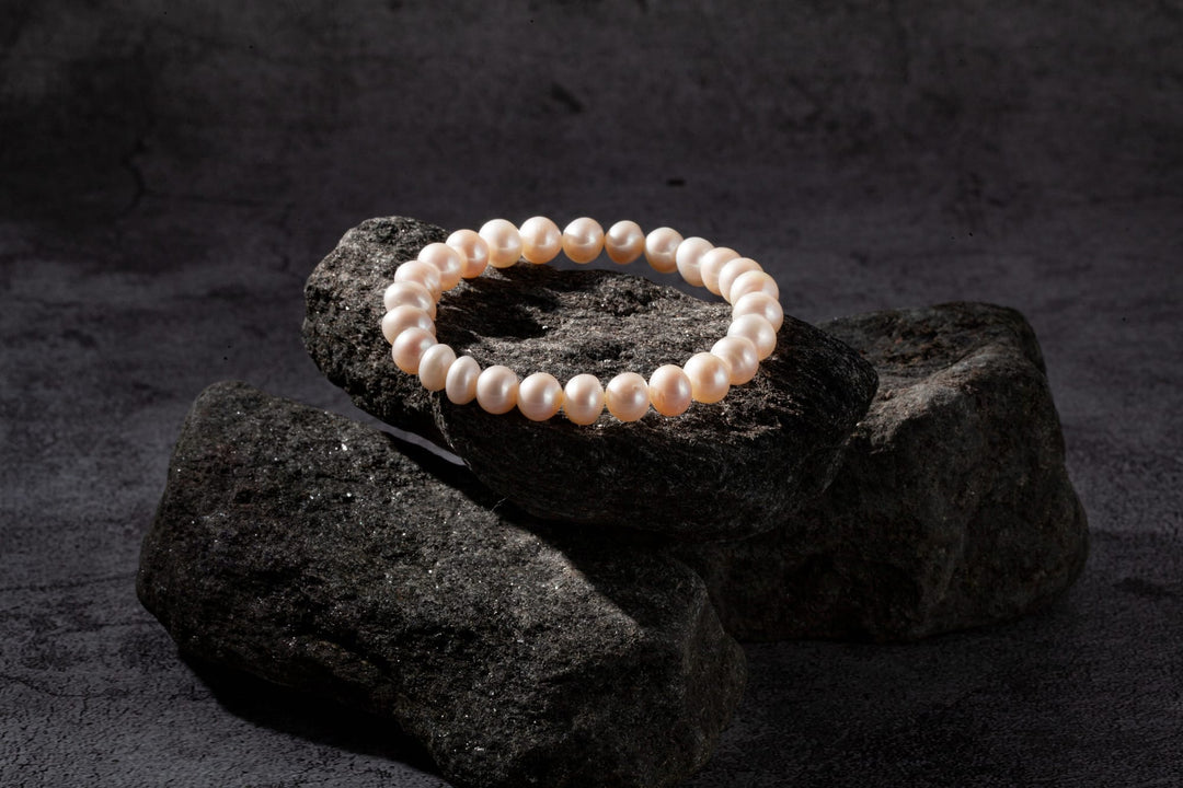 Elegant pearl bracelet displayed on dark rocks, showcasing lustrous pearls for fine jewelry lovers.
